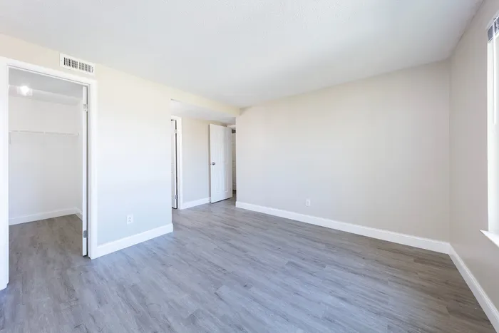 Spacious bedroom with vinyl wood flooring and large windows.