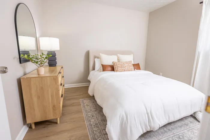 Spacious bedroom with hardwood flooring, large floor to ceiling windows, decorated with neutral bedding, orange pillows, and large rug. Explore pet-friendly studio, one-, and two-bedroom apartments in Cincinnati, OH. The Alcove offers upscale living with premium amenities near downtown. apartments for rent in Cincinnati OH, Cincinnati luxury apartments, pet-friendly apartments in Cincinnati, downtown Cincinnati apartments, one bedroom apartments Cincinnati, The Alcove Apartments Cincinnati