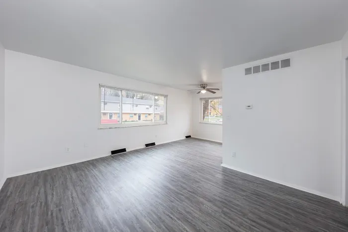 Spacious living room with large windows allowing natural light to fill the space, and ceiling fan.