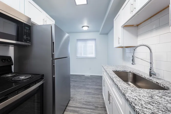 Open layout kitchen connected to the living room with granite countertops, stainless steel appliances, vinyl wood flooring, and large sink with extended faucet.