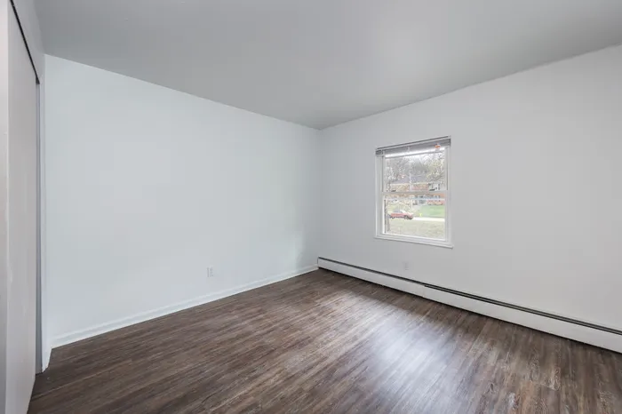 Spacious bedroom with vinyl wood flooring and large windows.