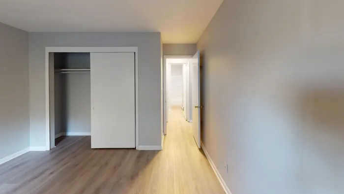 Modern apartment hallway with light wooden flooring and neutral-toned walls leading to an open closet.