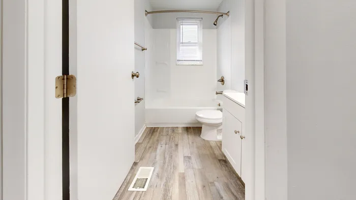 Bright and modern bathroom with a white tub, sleek fixtures, and wood-style flooring.
