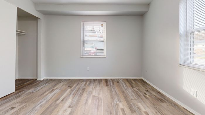 Sunlit room with elegant wood flooring and soft gray walls featuring a window and open closet space.