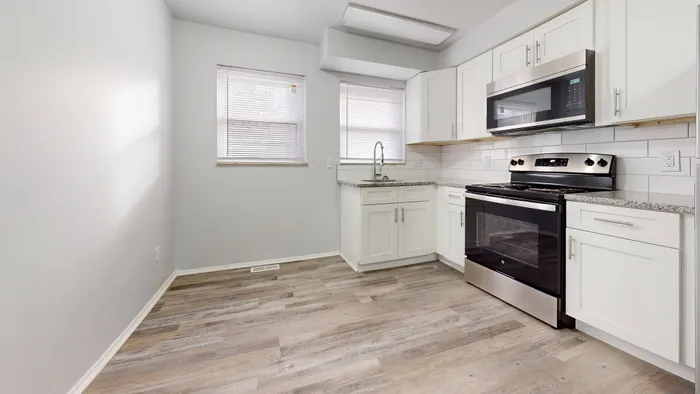 Sunlit modern kitchen with white cabinets, granite countertops, and stainless steel appliances.