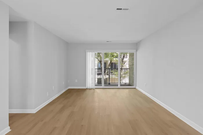 Elegant living room with bright natural light, sliding glass doors, and stylish wood flooring opening up to a cozy balcony view.