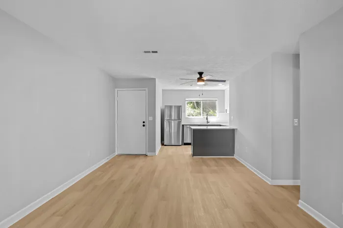 Bright and modern open-concept living area with stylish light wood flooring, stainless steel appliances, and a sleek ceiling fan, perfect for contemporary living.