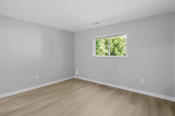 Bright and airy room with sleek laminated flooring and a large window offering a tranquil garden view.