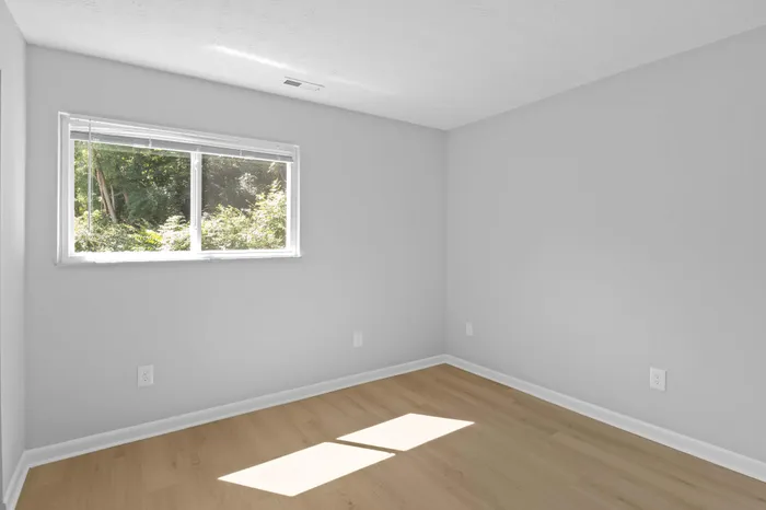 Bright and airy room with large window, showcasing natural light and a serene view of lush greenery.