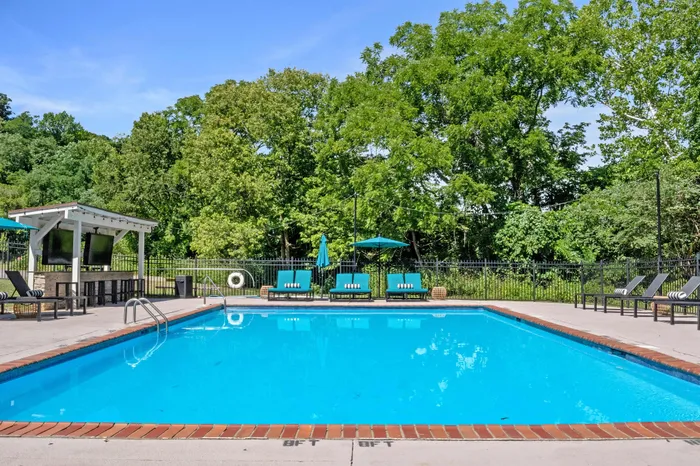 Inviting outdoor pool area surrounded by lush greenery, featuring comfortable lounge chairs and vibrant sun umbrellas for relaxation.