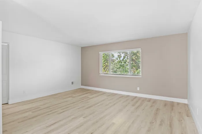 Bright and airy room featuring elegant wood flooring, neutral walls, and a large window with lush, green views.