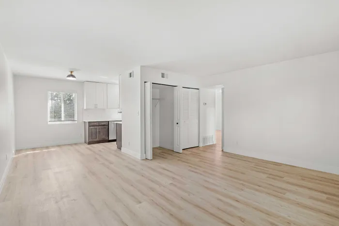 Bright, spacious living area with sleek wooden flooring and modern open-plan kitchen featuring pristine white cabinets.