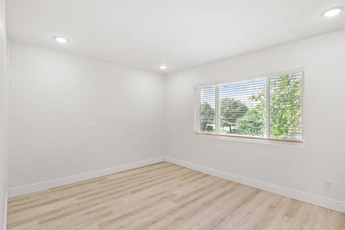 Bright and airy room with modern flooring and large window offering scenic views of lush greenery.