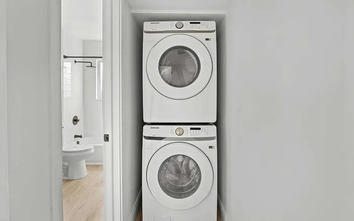 Modern apartment featuring a stacked in-unit washer and dryer next to a pristine bathroom, highlighting convenience and efficiency.