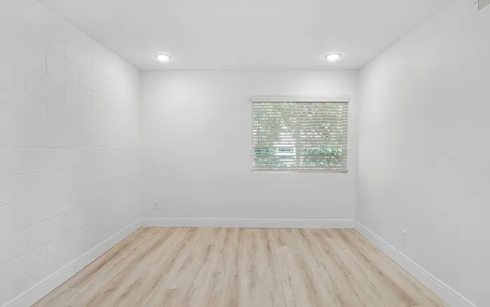 Bright minimalistic room with light wood flooring and a large window highlighting modern blinds.