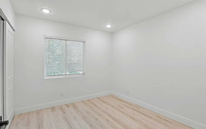 Bright and inviting empty room with elegant hardwood flooring and natural light filtering through stylish blinds.