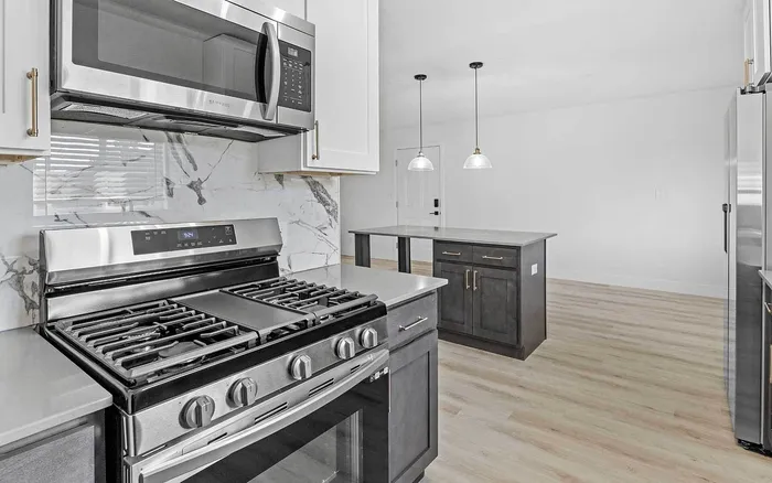 Modern kitchen with sleek stainless-steel appliances, elegant marble backsplash, and spacious island with pendant lighting.
