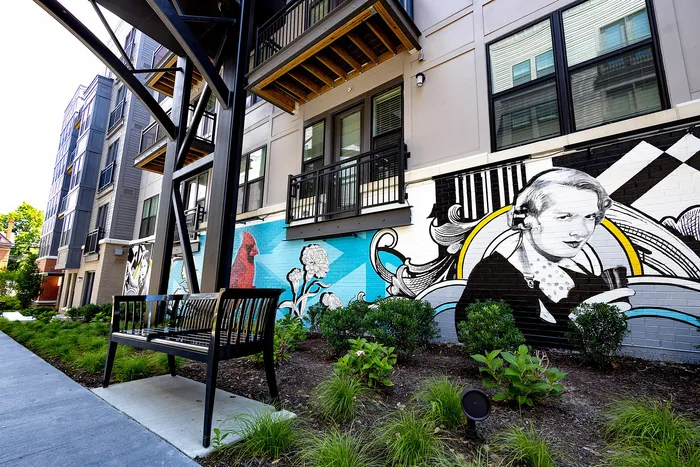 Modern apartment exterior featuring vibrant mural art with lush greenery and a stylish bench along a smooth walkway.