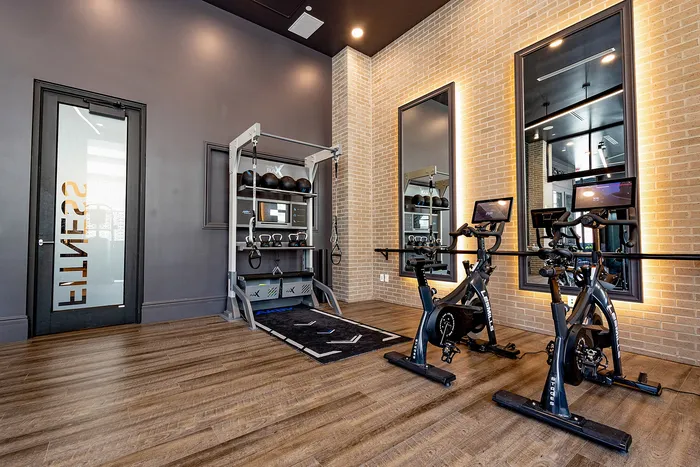 Modern gym interior featuring state-of-the-art exercise equipment, including spin bikes and a functional training station, with sleek wood flooring and stylish brick accents.