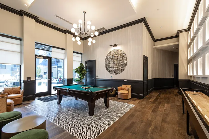 Luxurious game room with a billiard table, stylish chandelier, modern decor, and comfortable seating, perfect for entertaining in an upscale apartment complex.