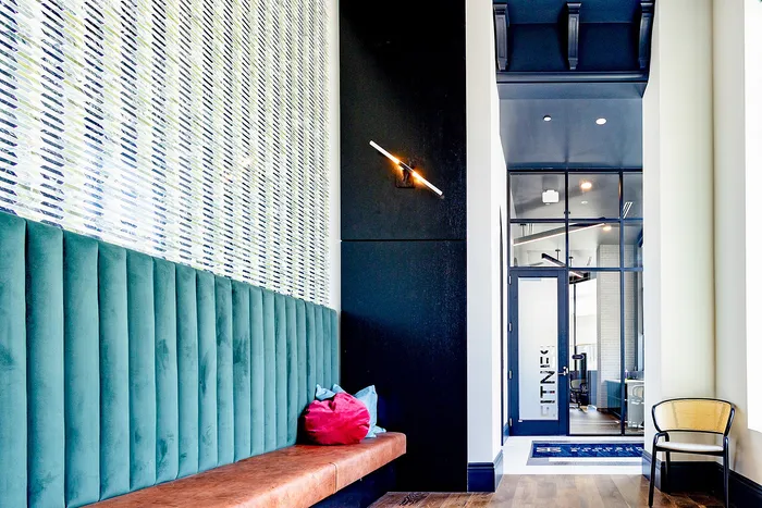 Stylish apartment lobby with teal paneling, modern wall light, and glass doors leading to a fitness center.