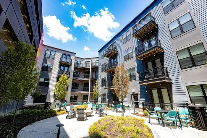 Modern apartment complex with balconies surrounding a vibrant courtyard featuring seating areas and lush landscaping under a clear blue sky.