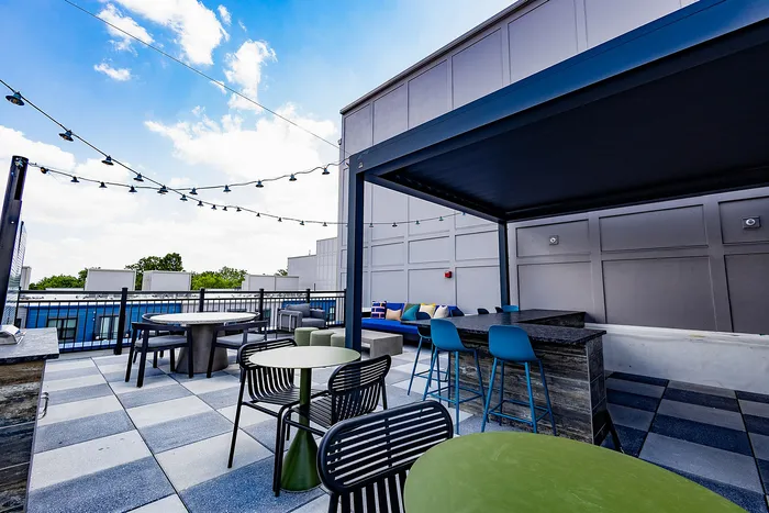 Chic rooftop terrace featuring modern seating, vibrant accents, and ambient string lighting under a clear blue sky.