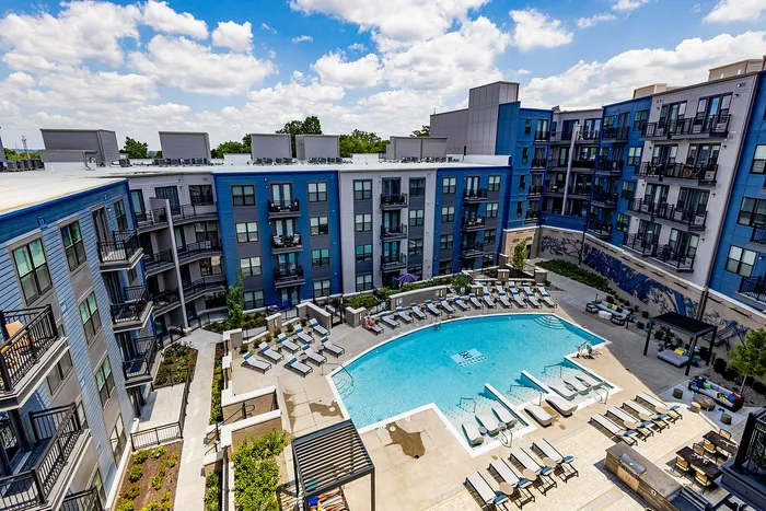 Luxurious apartment complex featuring a vibrant blue facade, multiple balconies, and a stunning resort-style pool area surrounded by sun loungers.