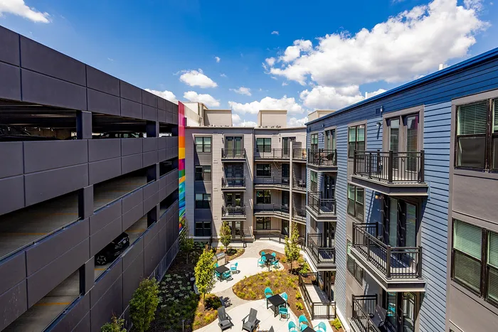 Vibrant apartment courtyard with modern architecture, colorful art accents, and inviting outdoor seating under a bright blue sky.