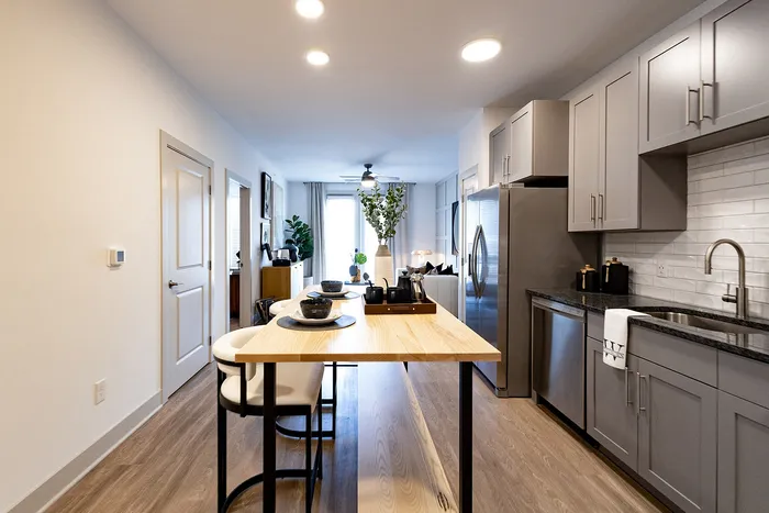 Modern, elegant kitchen and dining area with sleek gray cabinetry, stainless steel appliances, and a stylish island. Bright and inviting open layout with wood floors and tasteful decor.