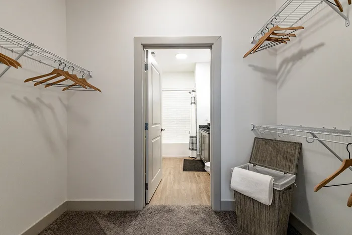 Spacious walk-in closet with ample shelving and a glimpse into a modern bathroom, featuring elegant wood flooring and a cozy ambiance.