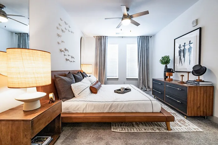 Elegant bedroom with modern decor, featuring a cozy bed, stylish wooden furniture, and natural light streaming through large windows.
