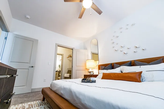 Bright and elegant bedroom featuring a cozy bed with plush pillows, stylish decor with wall accents, and warm ambient lighting.