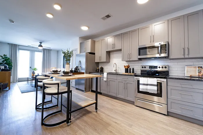 Modern kitchen with sleek gray cabinetry, stainless steel appliances, and a stylish island adjacent to a bright open living space.