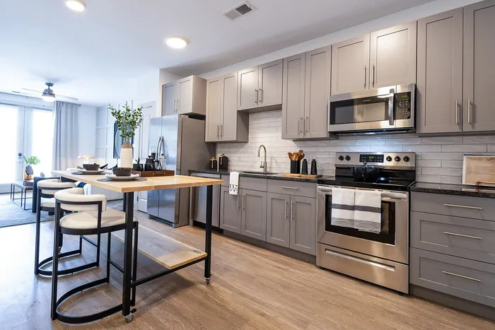 Modern kitchen with sleek gray cabinets, stainless steel appliances, and a stylish wooden island with seating, perfect for dining and entertaining.