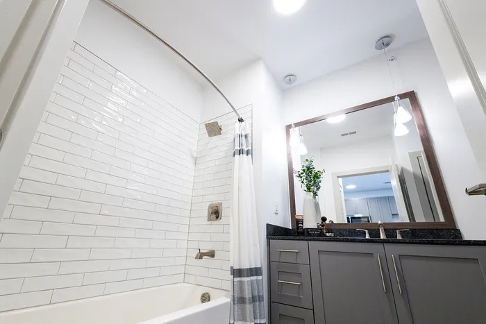 Modern bathroom featuring a sleek bathtub with subway tile, stylish vanity with a large framed mirror, and elegant lighting for a luxurious touch.
