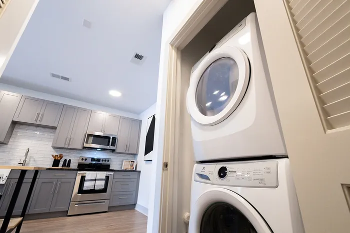 Modern apartment kitchen with sleek gray cabinets, stainless steel appliances, and in-unit stacked washer and dryer.