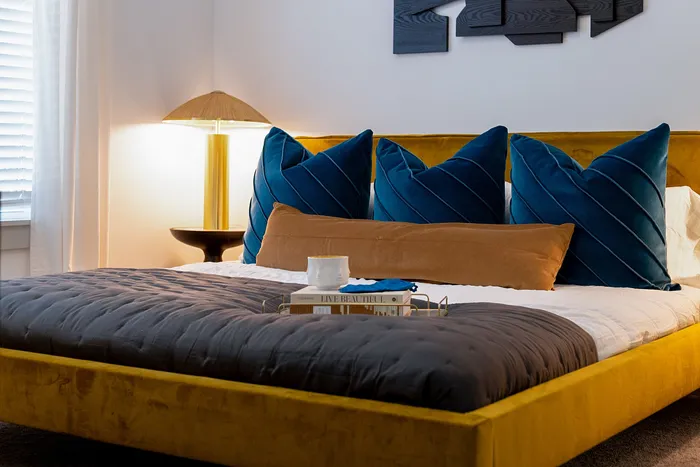 Inviting bedroom with a luxurious velvet bed, plush blue pillows, and modern decor accentuated by warm lighting.