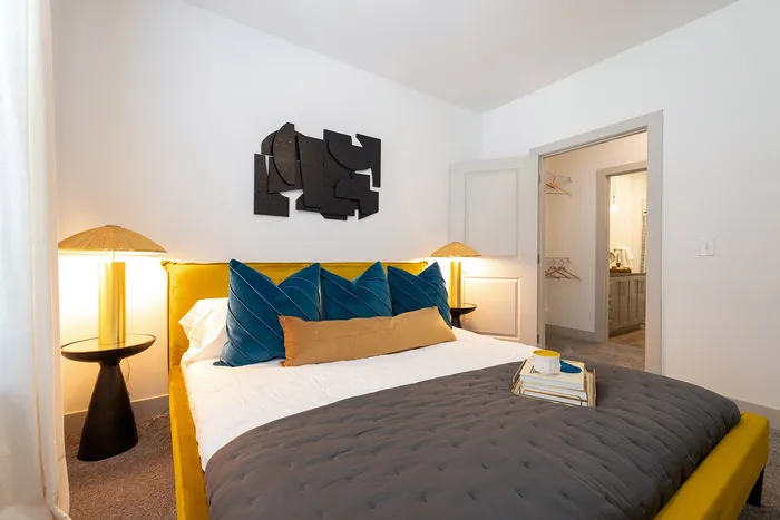 Bright and cozy bedroom with a stylish yellow bed frame, plush blue cushions, modern decor, and a soft ambient glow from chic lamps, offering a warm and inviting retreat.