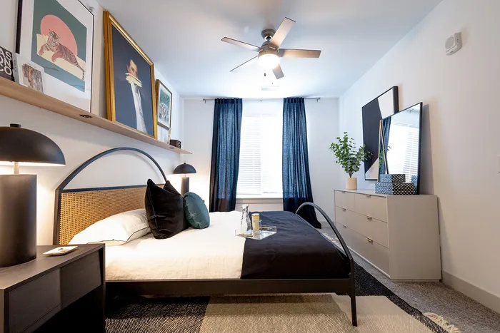 Modern bedroom featuring chic decor, stylish artwork, and cozy bedding, accented with a sleek ceiling fan and natural light for a serene ambiance.