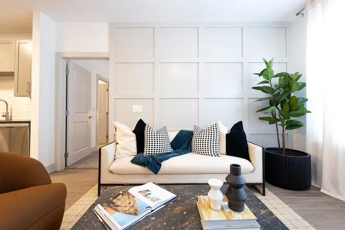 Inviting living room with sleek modern design, featuring a cozy beige sofa adorned with black and white pillows, a stylish coffee table, and a bright atmosphere enhanced by a large potted plant.