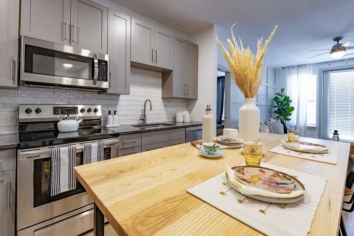 Modern kitchen with sleek cabinetry, stainless steel appliances, and a stylish wooden dining area adorned with elegant place settings and decorative vases.