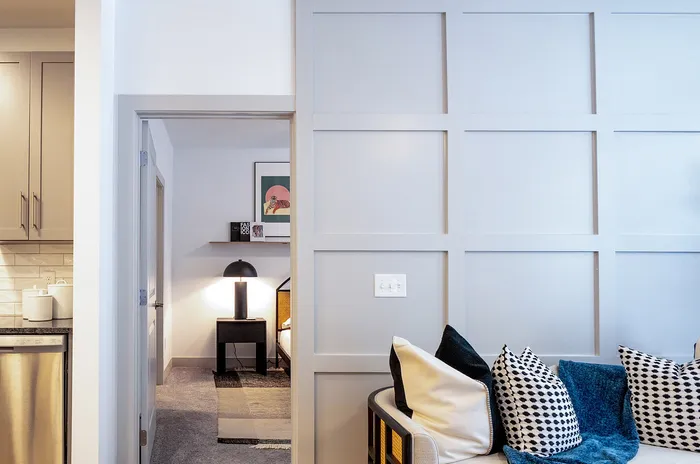 Inviting apartment interior showcasing a cozy sitting area with stylish cushions and a glimpse into a modern kitchen and snug bedroom.