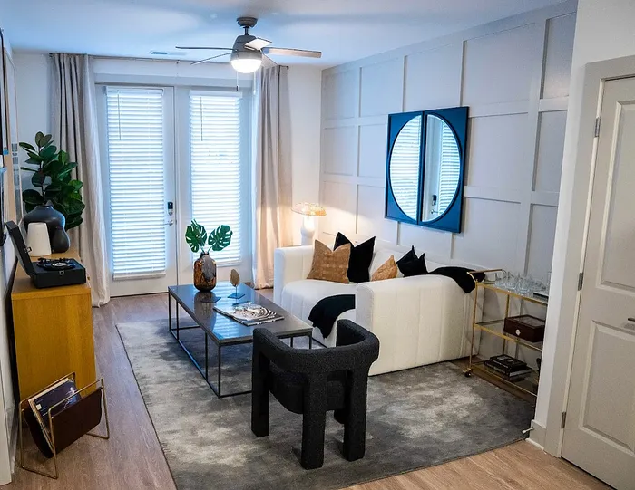 Chic living room with modern decor, plush white sofa, and stylish coffee table, illuminated by natural light through elegant French doors.