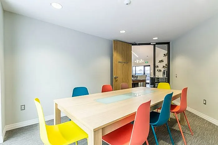 Vibrant meeting room with colorful chairs around a sleek wooden table, perfect for dynamic discussions and creative collaboration.