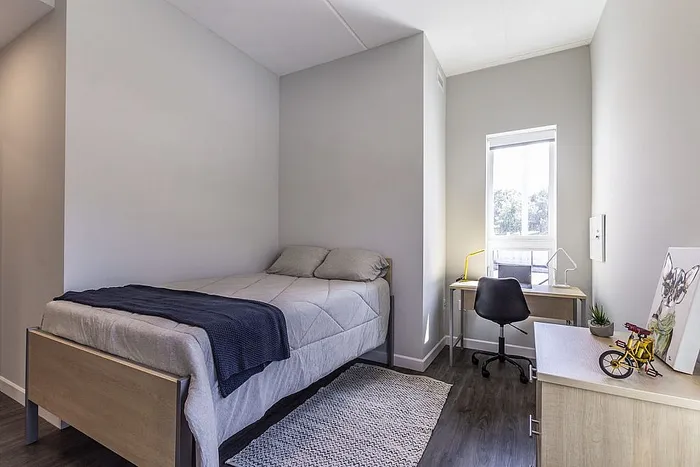 Bright and cozy bedroom featuring a comfortable bed, sleek desk setup by a sunlit window, and modern decor.
