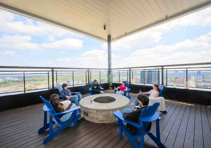 Rooftop terrace with a cozy fire pit and comfortable seating, offering stunning city skyline views under a partly cloudy sky.