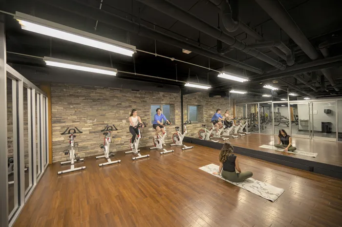 Modern fitness room with a row of stationary bikes, elegant wood flooring, and a mirrored wall reflecting a serene yoga practice space.