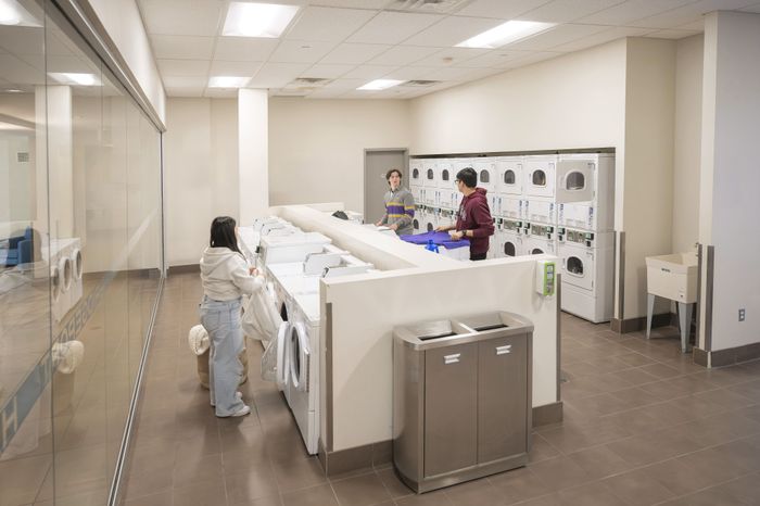 Modern apartment laundry room with bright lighting and multiple washing and drying machines, featuring residents doing laundry in a clean and organized space.