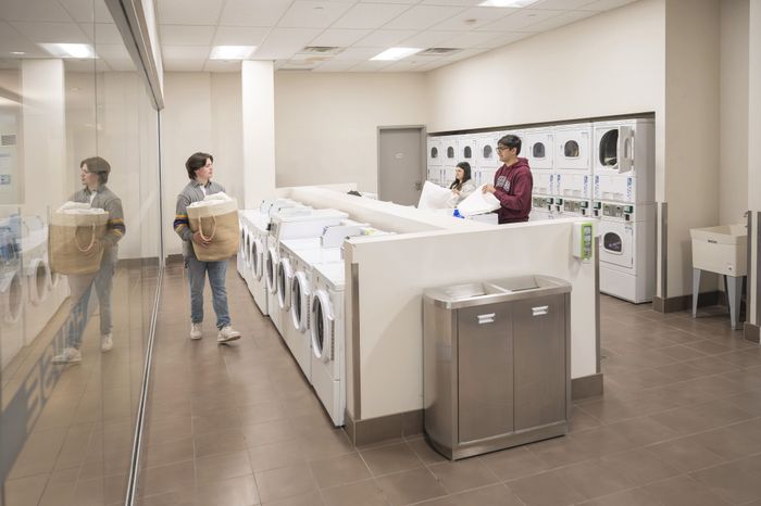 Bright, modern laundry room featuring multiple high-efficiency washers and dryers, with a convenient folding area and sleek design.